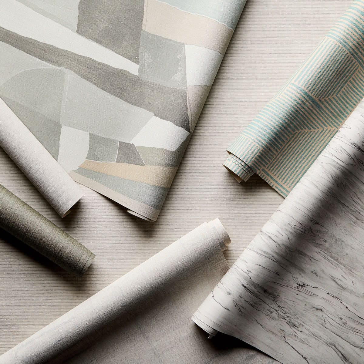 Rolls of patterned and textured wallpaper fanned out across a papered surface